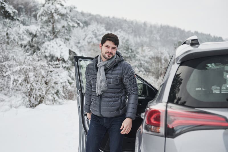 Un type avec une longue écharpe au cou sort de la voiture pour faire une promenade dans la forêt hivernale enneigée