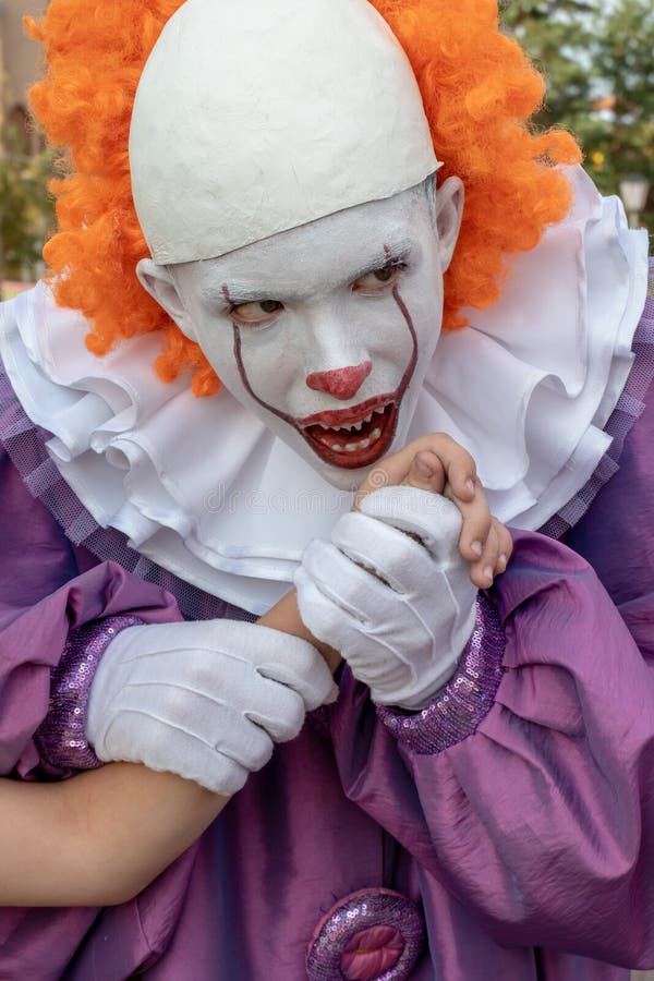 Un type en costume de clown effrayant avec des dents aiguës tient la main de quelqu'un d'autre et fait semblant de vouloir la mor photo libre de droits Un type en costume de clown effrayant avec des dents aiguës tient la main de quelqu'un d'autre et fait semblant de vouloir la mor photo libre de droits
