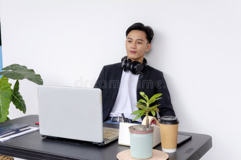 Un tânăr profesionist concentrat într-un birou de acasă modern, care lucrează la un laptop cu căști în jurul gâtului și care se în royalty free stock image