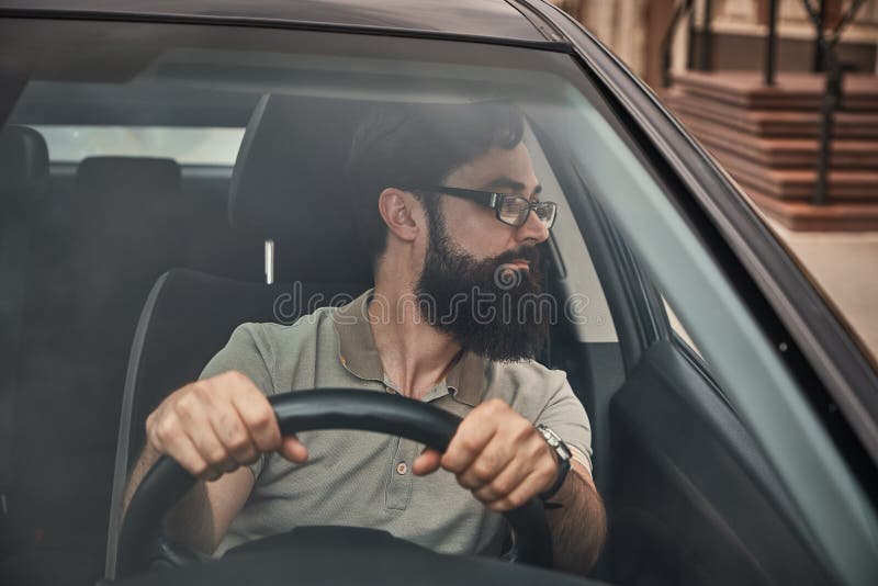Un uomo barbuto moderno che conduce un'automobile immagine stock Un uomo barbuto moderno che conduce un'automobile immagine stock