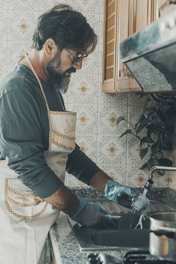 Un uomo che lava i piatti a casa in cucina dopo pranzo. marito che aiuta la moglie a pulire la casa. appartamento domestico intern immagine stock