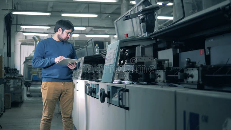 Un uomo controlla le apparecchiature di stampa che funzionano, fine su