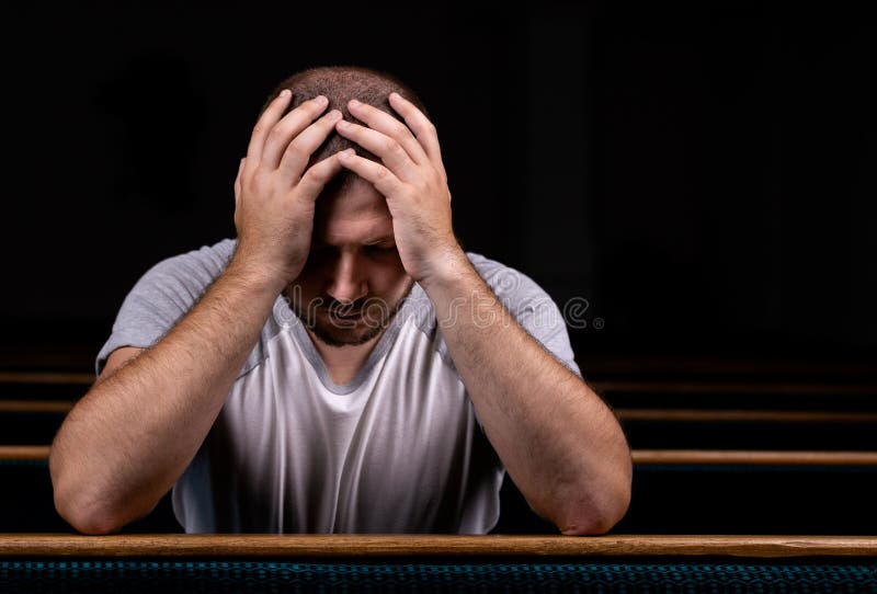 Un uomo cristiano triste in camicia bianca è sedentesi e pregante con il cuore umile nella chiesa immagine stock Un uomo cristiano triste in camicia bianca è sedentesi e pregante con il cuore umile nella chiesa immagine stock