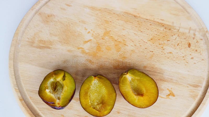 Un uomo dispone metà delle prugne affettate su una tavola gialla di legno. grosse prugne blu scure su un piatto bianco. bei frutti
