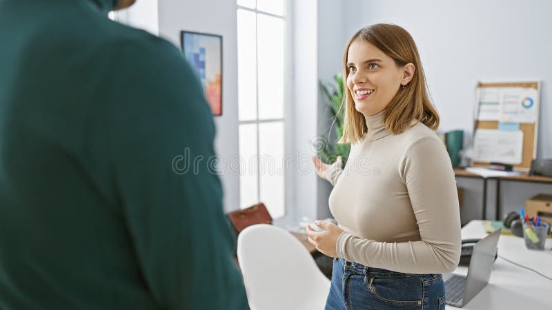 Un uomo e una donna convergono in un ufficio luminoso con la donna sorridendo incarnando fiduciosamente il lavoro di squadra e la fotografia stock
