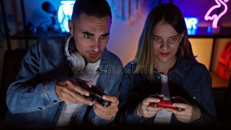 Un uomo e una donna a fuoco impegnati in videogiochi competitivi in una stanza per videogiochi scura di notte fotografia stock libera da diritti