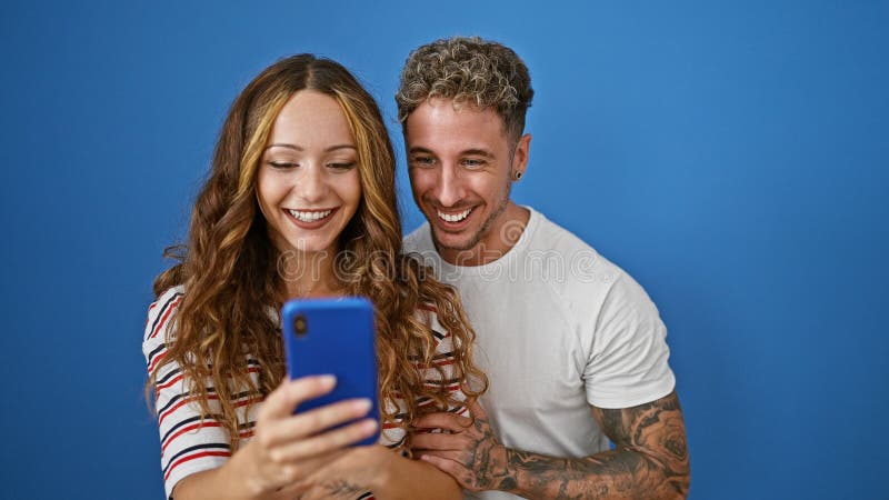 Un uomo e una donna sorridenti condividono un momento gioioso insieme su uno sfondo blu che cattura un selfie fotografie stock