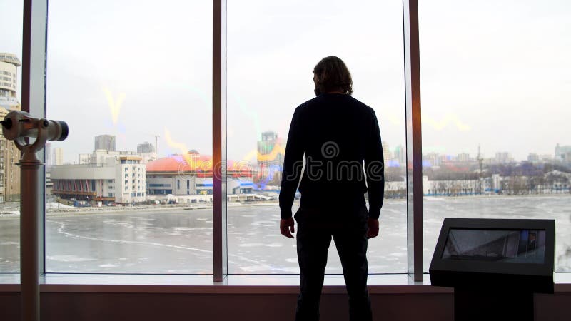 Un uomo guarda una bella vista della città e un lago ghiacciato dal ponte di osservazione. media. vista posteriore di un giovane