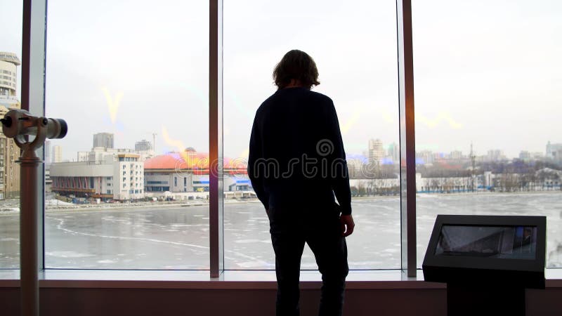 Un uomo guarda una bella vista della città e un lago ghiacciato dal ponte di osservazione. media. vista posteriore di un giovane