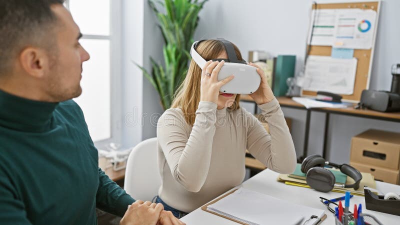 Un uomo osserva una donna che indossa una cuffia di realtà virtuale in un ufficio moderno che simboleggia un lavoro innovativo fotografie stock