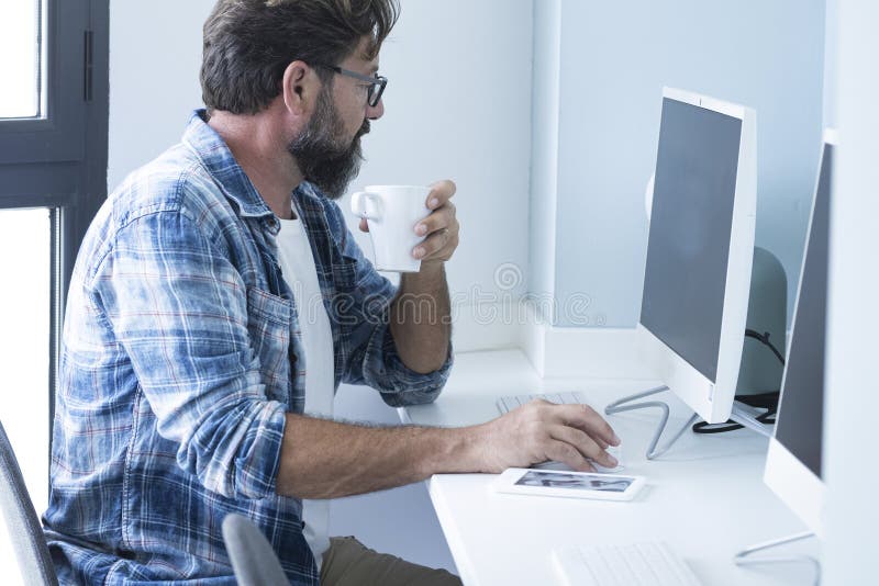 Un uomo seduto alla scrivania che lavora al computer e beve caffè. attività di lavoro indipendente professionale interno. fotografia stock libera da diritti