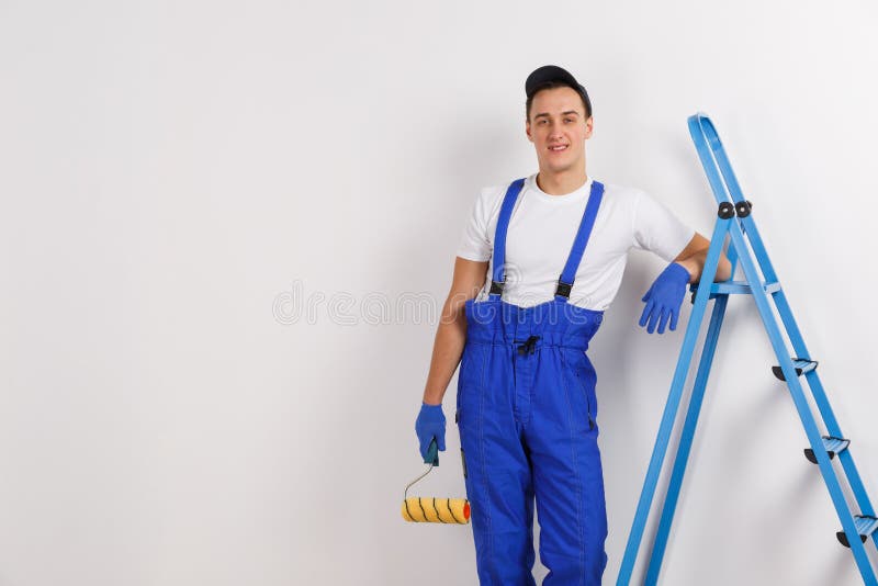 Un uomo sorridente è un costruttore, pendendo contro una scala, tenente un rullo della costruzione in sua mano fotografia stock libera da diritti Un uomo sorridente è un costruttore, pendendo contro una scala, tenente un rullo della costruzione in sua mano fotografia stock libera da diritti