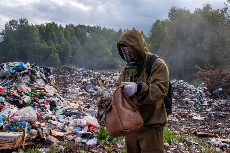 Un uomo in una maschera antigas esamina il contenuto della borsa Il lavoratore è nello scarico Intorno alle ustioni e fuma l'immo fotografie stock Un uomo in una maschera antigas esamina il contenuto della borsa Il lavoratore è nello scarico Intorno alle ustioni e fuma l'immo fotografie stock
