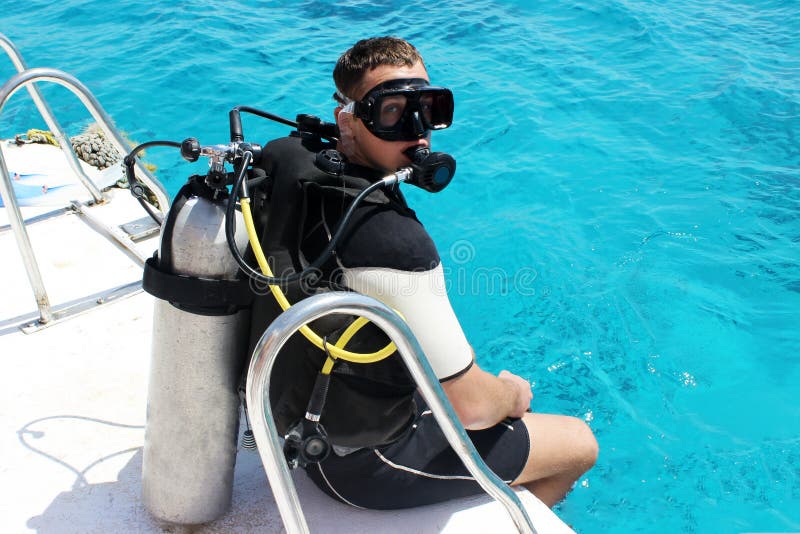 Un uomo in una muta umida, con un autorespiratore, la maschera e un pallone Un operatore subacqueo in attrezzatura per l'immersio fotografie stock Un uomo in una muta umida, con un autorespiratore, la maschera e un pallone Un operatore subacqueo in attrezzatura per l'immersio fotografie stock
