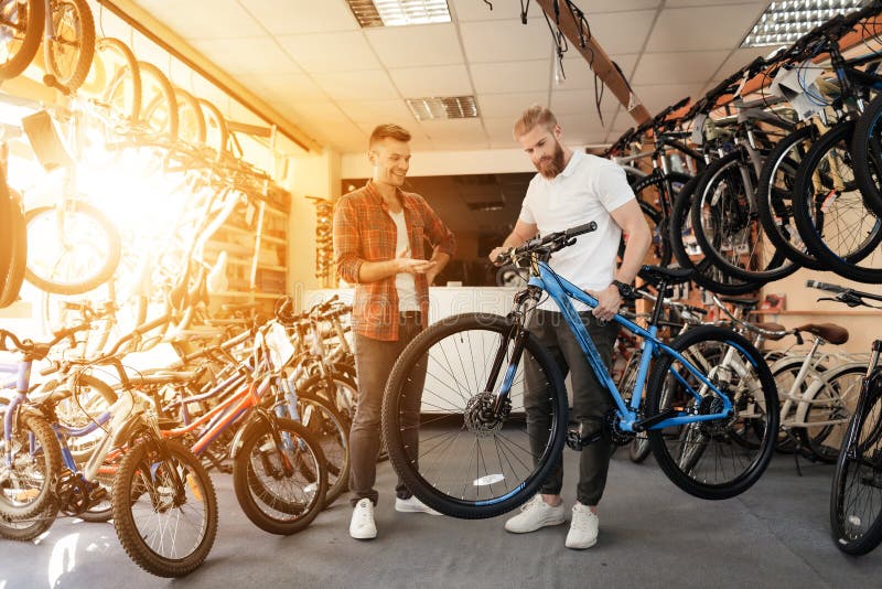 Un vendeur à un magasin de cycles aide un jeune acheteur à choisir un nouveau vélo de montagne images libres de droits
