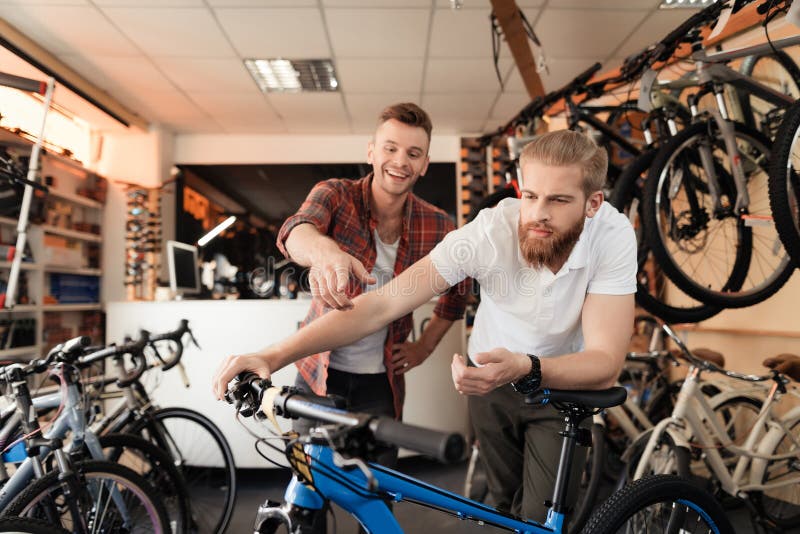 Un vendeur à un magasin de cycles aide un jeune acheteur à choisir un nouveau vélo de montagne image libre de droits