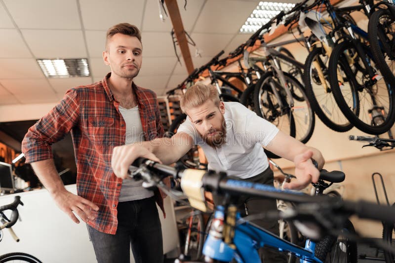 Un vendeur à un magasin de cycles aide un jeune acheteur à choisir un nouveau vélo de montagne photographie stock