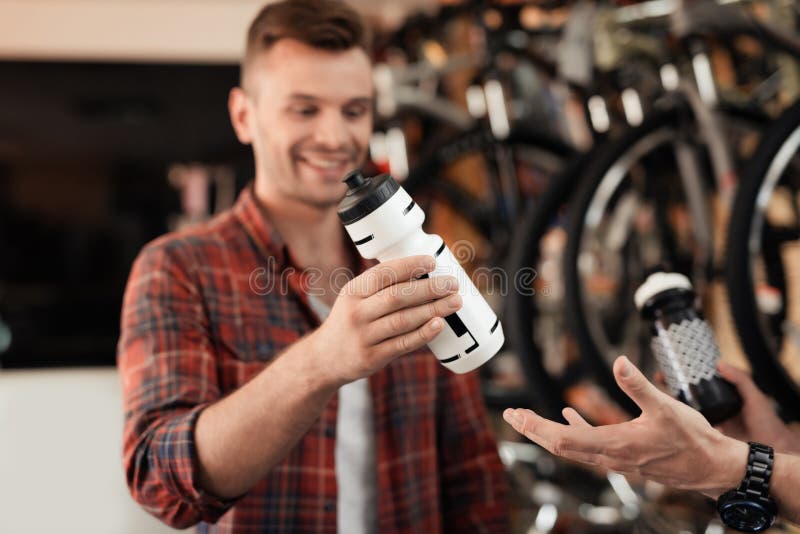 Un vendeur à un magasin de cycles aide un jeune acheteur à choisir une bouteille d'eau pour des tours de vélo photos stock