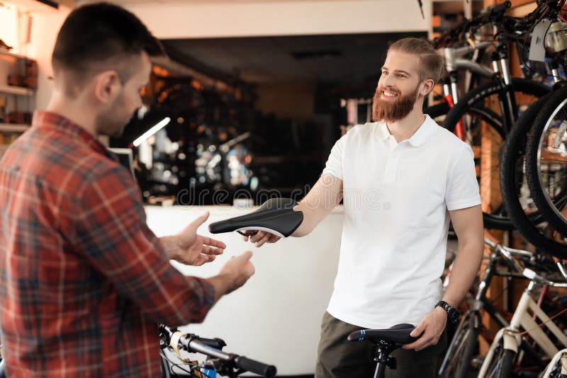 Un vendeur à un magasin de cycles aide un jeune acheteur à choisir une selle pour une bicyclette photographie stock