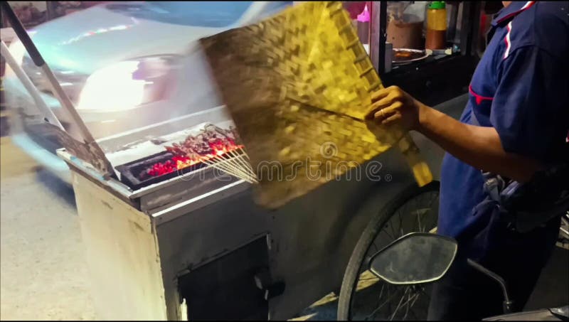Un venditore di satay di pollo della Madura sta cucinando in un carretto di cibo per strada di notte. stock footage