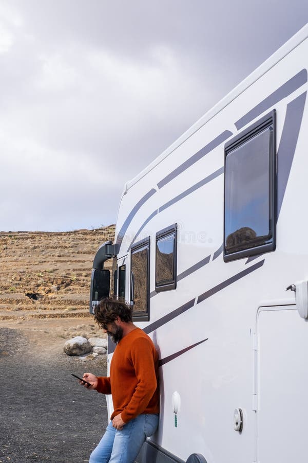 Un viaggiatore che usa un'app telefonica fuori da un moderno grande camper van per pianificare un viaggio in macchina e la prossim fotografia stock