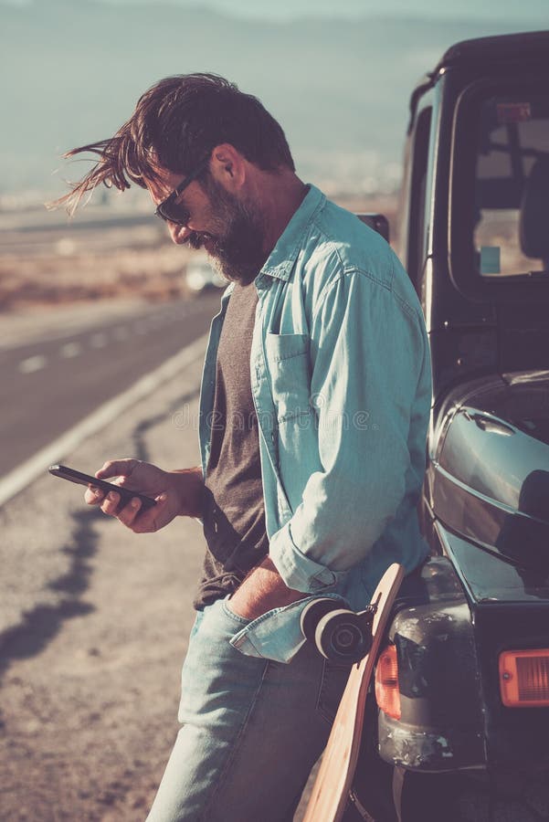 Un viaggiatore che utilizza una connessione telefonica e di roaming all'esterno dell'auto con una lunga strada panoramica in backg fotografia stock libera da diritti
