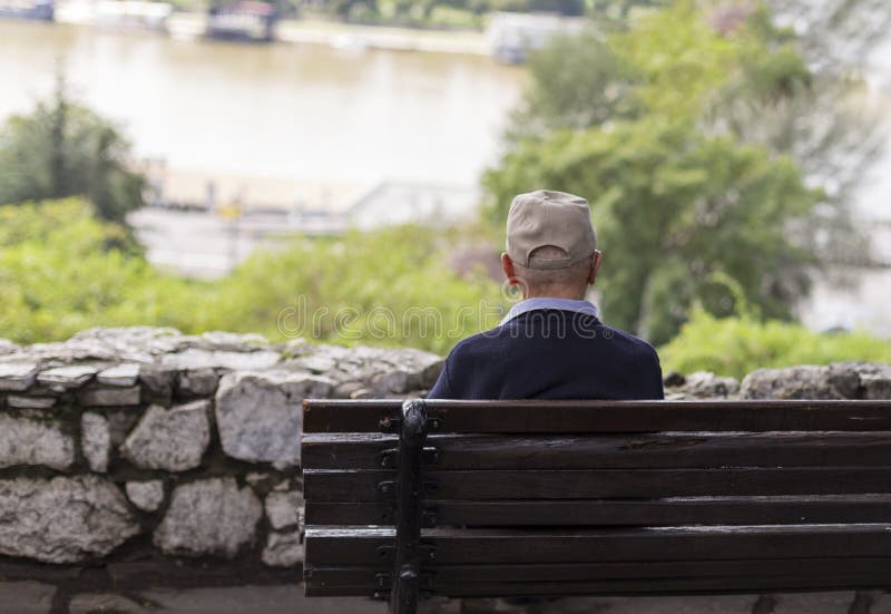 Un vieil homme seul s'asseyant sur un banc en parc, regardant la rivière