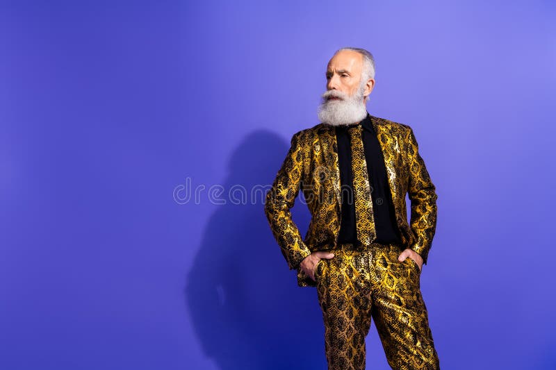 Un vieil homme élégant en costume d'or posant avec confiance sur un fond violet solide exprimant le charisme et photos stock