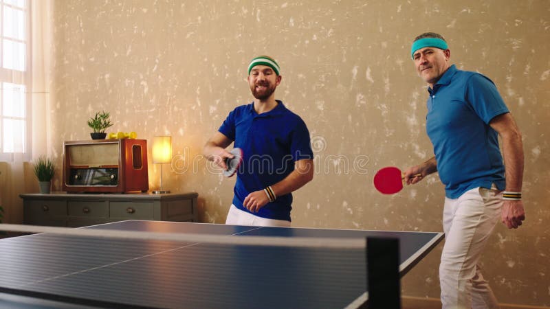 Un viejo bien parecido y un jovencito carismático jugando juntos como un equipo en la mesa de ping-pong atrapan el balón almacen de metraje de vídeo