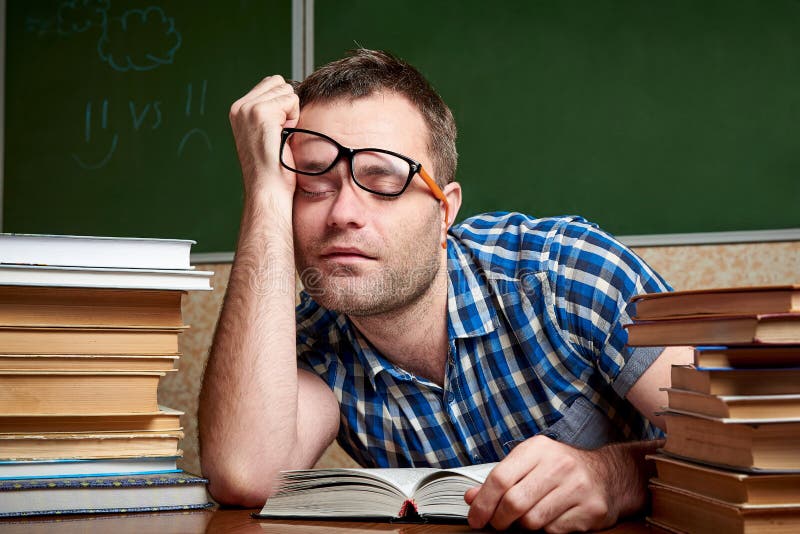 Un étudiant en désordre fatigué et torturé en verres dort à une table avec des piles de livres image stock Un étudiant en désordre fatigué et torturé en verres dort à une table avec des piles de livres image stock
