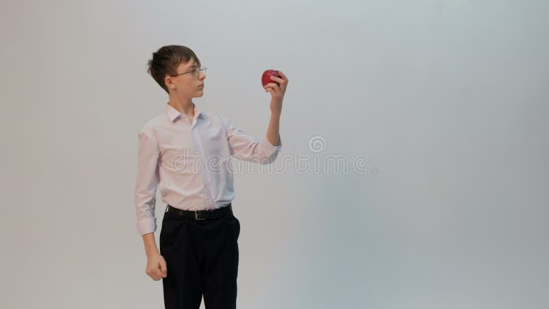 Un étudiant ou un écolier avec des verres et une chemise blanche compare un poing à une pomme rouge Un adolescent d'aspect amusan