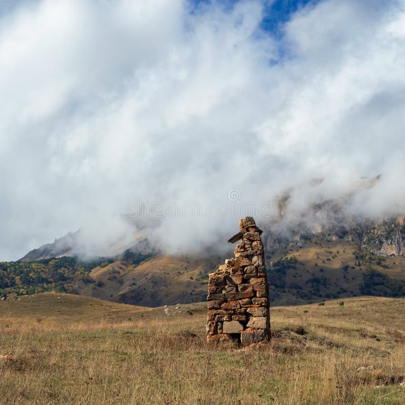 An ancient stone idol on the background of misty mountains. Tombstones made of stone. Stur-Digora region. North Ossetia. An ancient stone idol on the background of misty mountains. Tombstones made of stone. Stur-Digora region. North Ossetia.