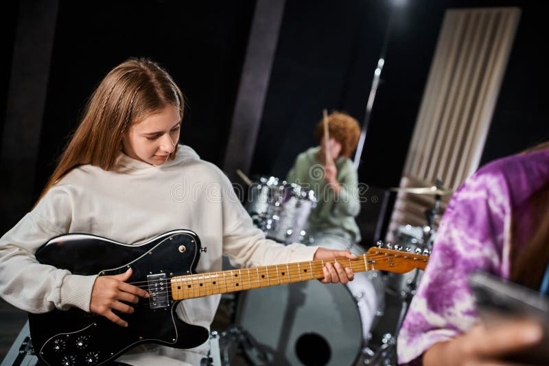 adorable blonde teenage girl in casual attire playing guitar next to her talented friends in studio, stock photo. adorable blonde teenage girl in casual attire playing guitar next to her talented friends in studio, stock photo