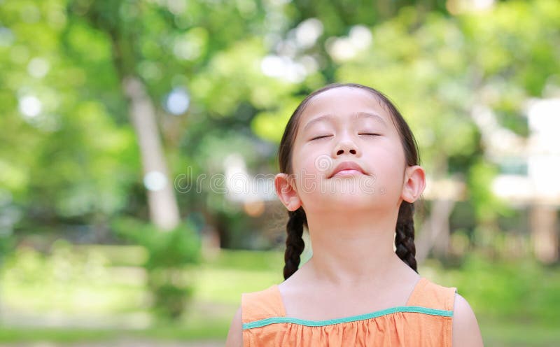 Una bambina asiatica, pacifica, chiude gli occhi in giardino con aria fresca dal respiro della natura Ritratto di bambino in verd