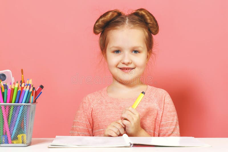 Una bambina carina seduta al tavolo e disegna Sfondo rosa Chiudi fotografia stock Una bambina carina seduta al tavolo e disegna Sfondo rosa Chiudi fotografia stock