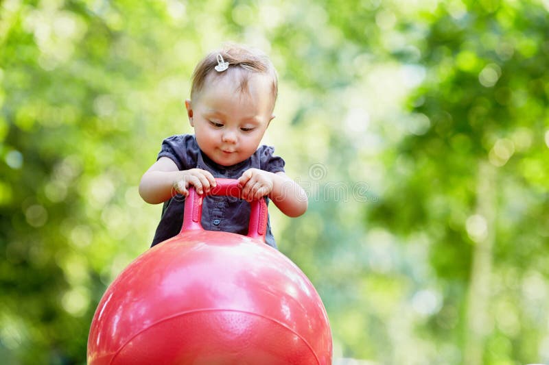 Una bambina gioca con la palla rossa per saltare su fotografia stock