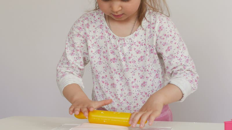 Una bambina rotola allegro la pasta su una tavola con un matterello