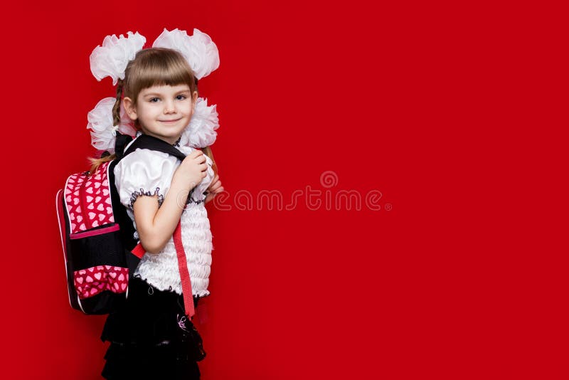 Una bambina sveglia dello smilng in uniforme scolastico e nel bianco si piega con uno zaino su fondo rosso Di nuovo al banco fotografia stock Una bambina sveglia dello smilng in uniforme scolastico e nel bianco si piega con uno zaino su fondo rosso Di nuovo al banco fotografia stock