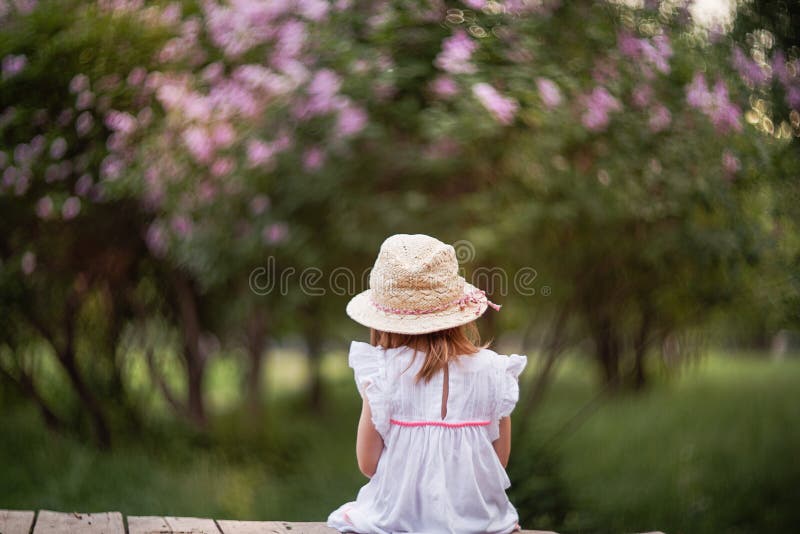 Una bambina è sedentesi ed esaminante un cespuglio lilla fotografie stock Una bambina è sedentesi ed esaminante un cespuglio lilla fotografie stock