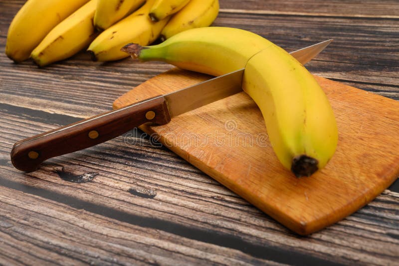 Una banana gialla matura tagliata in due con un coltello su una tavola di legno su uno sfondo di legno Chiudi fotografia stock Una banana gialla matura tagliata in due con un coltello su una tavola di legno su uno sfondo di legno Chiudi fotografia stock