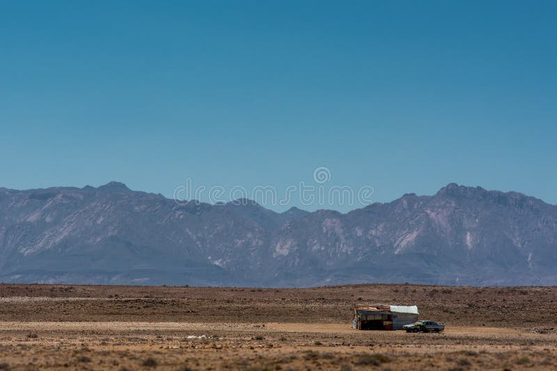 Una baracca e un'automobile sole in mezzo di vasto e paesaggio namibiano asciutto, contro la montagna di Brandberg immagini stock Una baracca e un'automobile sole in mezzo di vasto e paesaggio namibiano asciutto, contro la montagna di Brandberg immagini stock