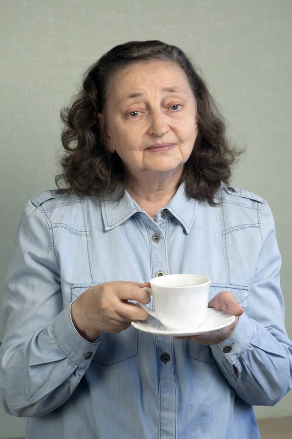 Una bella anciana de unos 65 años se regocija, sonríe En manos de una taza de té o café fotografía de archivo Una bella anciana de unos 65 años se regocija, sonríe En manos de una taza de té o café fotografía de archivo