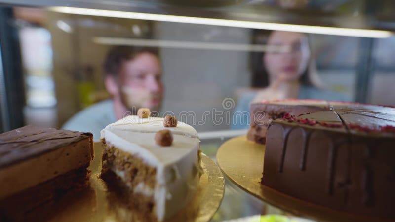 Una bella coppia sorride e sceglie un dessert. un uomo e una donna decidono quale torta o pasta comprare per il tè archivi video