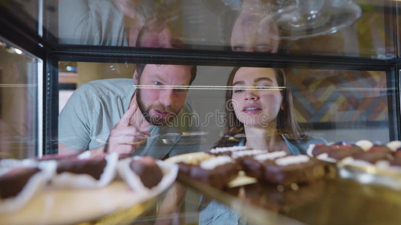 Una bella coppia sorride e sceglie un dessert. un uomo e una donna decidono quale torta o pasta comprare per il tè archivi video