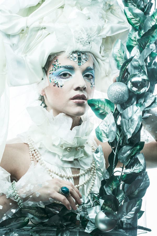Una bella donna in costume per il carnevale natalizio si pone in una cornice di decorazioni natalizie e foglie d'argento. fotografie stock