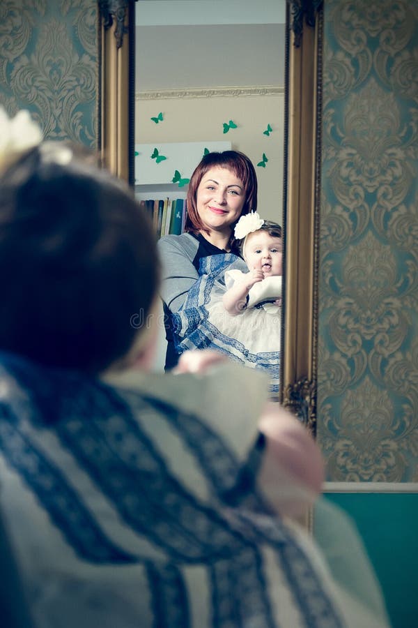 Una bella madre sostiene un piccolo bambino in suoi vestito e cappello fotografia stock Una bella madre sostiene un piccolo bambino in suoi vestito e cappello fotografia stock