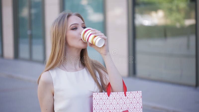 Una bella ragazza cammina con i pacchetti dal deposito e beve il caffè Riuscito acquisto