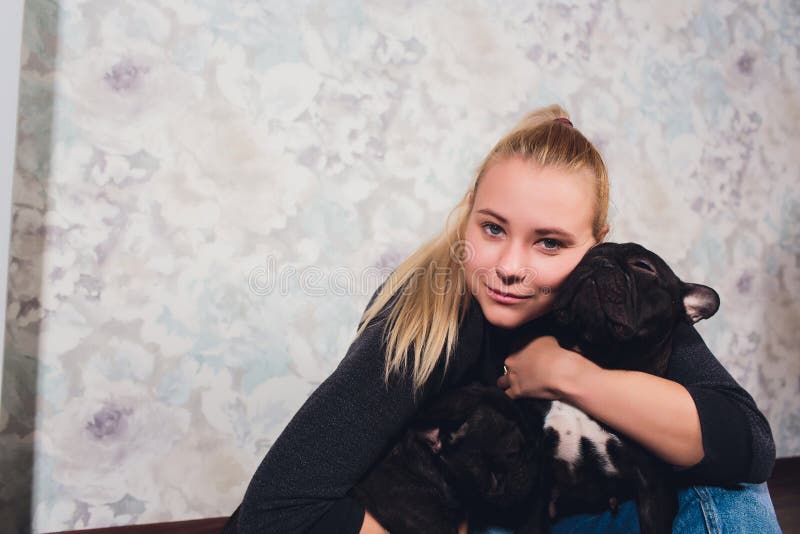Una bella ragazza si siede e tiene molto piccolo cucciolo di un cane del bulldog francese immagini stock Una bella ragazza si siede e tiene molto piccolo cucciolo di un cane del bulldog francese immagini stock