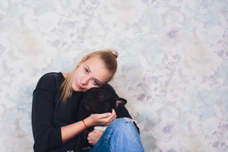Una bella ragazza si siede e tiene molto piccolo cucciolo di un cane del bulldog francese fotografia stock Una bella ragazza si siede e tiene molto piccolo cucciolo di un cane del bulldog francese fotografia stock