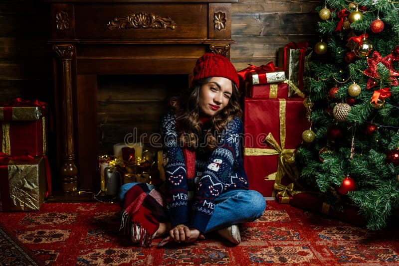 Una bellissima brunetta siede sotto un albero di Natale sullo sfondo di nuove decorazioni. immagini stock